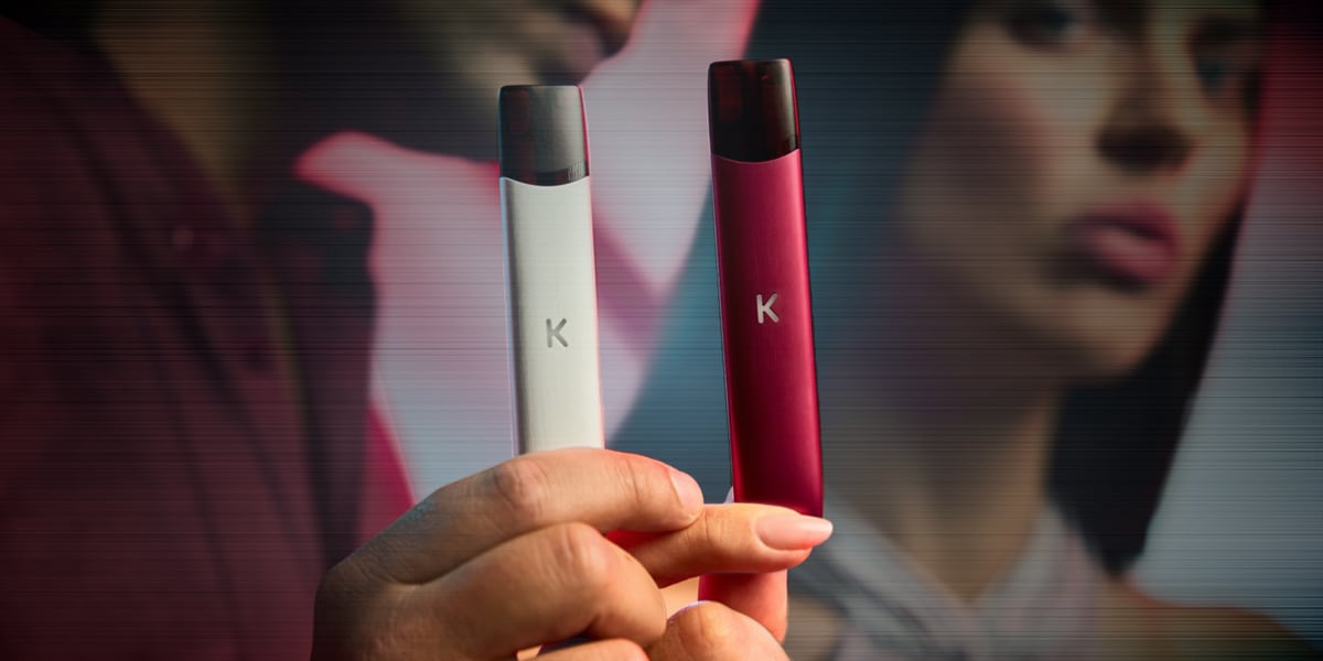 Zwei K Vape Pod-Systeme in Weiss und Rot, 20 mg, in der Hand vor unscharfem Hintergrund